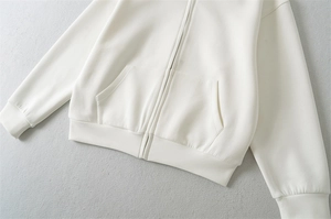 Détail d'un sweat à capuche ivoire zippé montrant le tissu lisse et l'ourlet côtelé