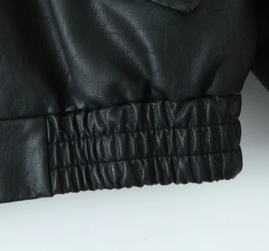 Détail macro de l'ourlet élastique et du cuir noir texturé de cette veste baseball