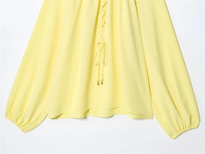 Details der hellgelben Laternenärmel-Bluse mit Kordelzug am Ausschnitt und Goldperlen