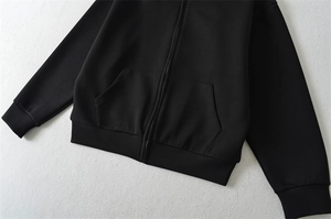 Détail d'un sweat à capuche noir zippé avec poignets côtelés et poches latérales
