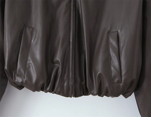 Detail of vintage brown leather jacket showing metal zipper pockets and elastic hem
