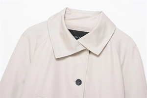 Detail of a beige short trench coat collar with lapels and a contrasting black button
