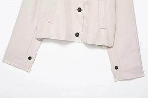 Detail view of off-white short trench coat with large black buttons and side pockets