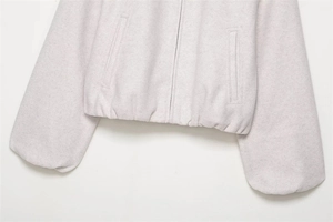 Detail of light gray fleece bomber jacket showing metal zipper and elastic hemline