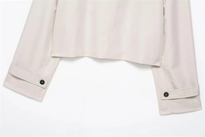 Detail of beige short trench coat featuring adjustable cuff straps and black buttons