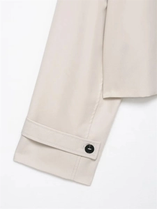 Detail of short trench coat cuff showing black button and precise stitching on beige fabric