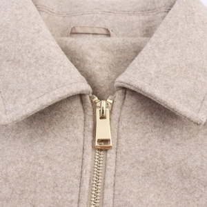 Detailed close-up of a premium gold metal zipper on a beige wool jacket fabric