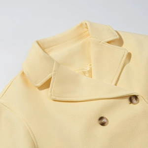 Détail des boutons croisés et du col à revers sur un manteau en laine jaune