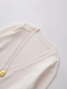 Detailed view of white V-neck knit top featuring a unique irregular gold button decoration