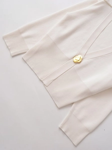 Detail of cream knit cardigan featuring a unique liquid gold metallic button and V-neckline