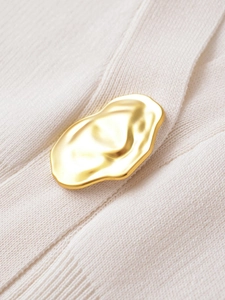 Close-up of a golden irregular lava button on a beige ribbed knit sweater top