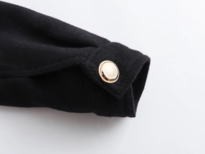 Detail shot of a golden metal button with grid texture on a black fabric sleeve cuff