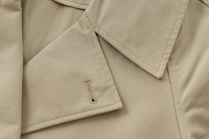 Detailed close-up of khaki trench jacket lapel, stitching, and precise buttonhole texture