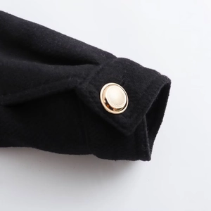 Women's black wool coat sleeve detail featuring a textured bright gold metal button