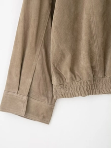 Detailed close-up of brown suede jacket showing elastic hem and precise stitching