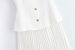 Détail d'une robe plissée blanche montrant des boutons dorés et la texture du tissu