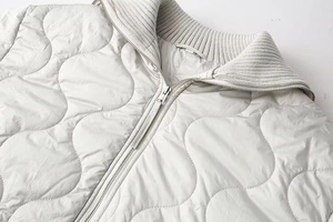 Détail de veste matelassée grise avec motifs de vagues et col montant en maille