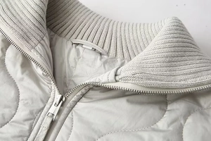 Détail d'une veste matelassée grise avec fermeture éclair argentée et col en maille