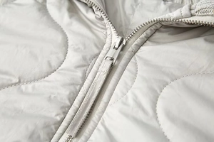 Détail de la fermeture éclair en métal argenté et du motif matelassé ondulé sur la veste