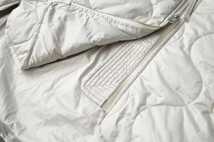 Gros plan sur la texture matelassée ondulée et le zip argenté du manteau gris clair
