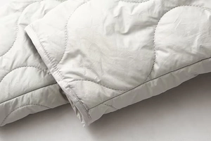 Gros plan d'une veste matelassée gris clair avec surpiqûres courbées et texture du tissu