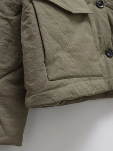 Detailed view of olive green quilted jacket featuring onion stitching and cargo pockets