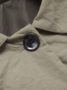 Detailed close-up of a black four-hole button and precision stitching on the khaki jacket