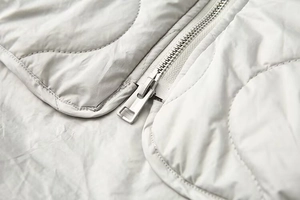Détail de la fermeture éclair en métal argenté sur une veste matelassée gris clair