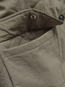 Detail of olive green quilted jacket featuring wavy patterns and a large utility pocket