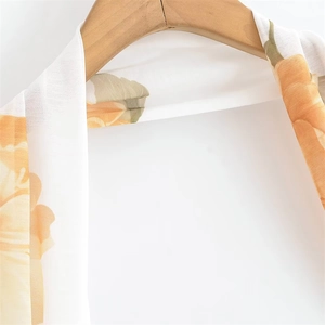 Détail d'une robe en mousseline blanche à motifs floraux oranges sur un cintre