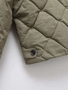 Detailed view of olive green quilted jacket featuring diamond stitching and button cuffs