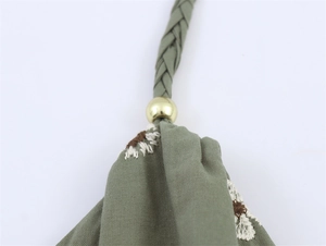 Detail aus grünem Stoff mit gestickten Gänseblümchen und goldener Metallperle