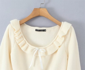 Detailed view of cream-colored knit sweater with lace neckline and white ribbon bow