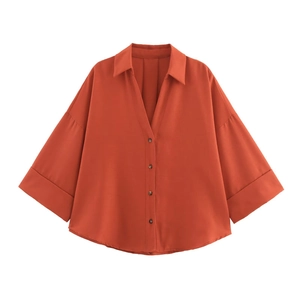 Detail of rust red loose fit blouse with rolled cuffs and button closure design