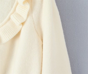 Detailed close-up of cream knit sweater showing ruffled neckline and ribbon tie textures