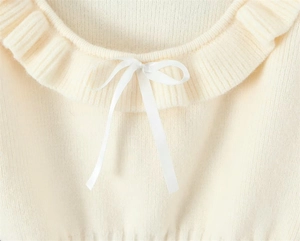 Detailed view of the crew neck with lace trim and ribbon bow on cream knit top