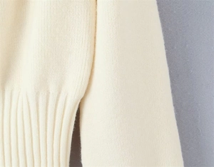 Close-up of cream knit sweater showing fine texture and ribbed hem detail