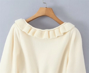 Detail of the ruffle neckline and vertical ribbing texture on this beige knit sweater