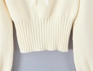 Detail of cream knit sweater showing elastic ribbed hem and delicate white ribbon trim