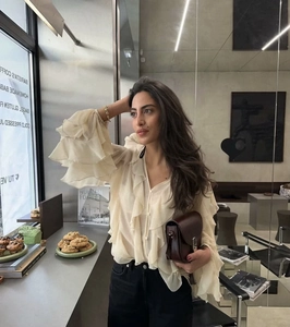 Detailed view of beige ruffled blouse with layered texture and sleek leather crossbody bag
