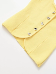 Dettaglio del top in maglia gialla con bottoni in metallo argento e trama fine