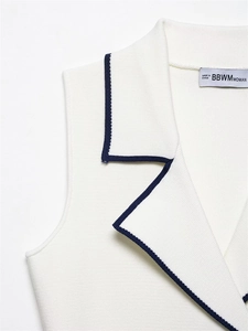 Close-up of knit vest collar with dark blue trim and brand tag on white fabric