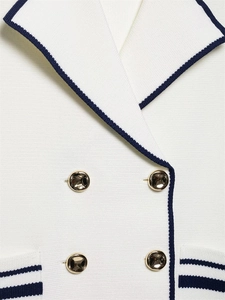 Detailed close-up of white knit vest with navy trim and gold buttons on the pockets