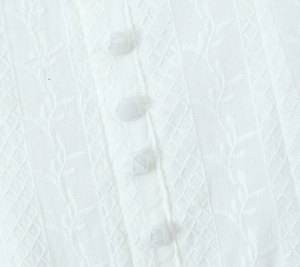 Detail of white cotton mini dress featuring floral embroidery and covered buttons