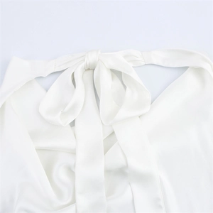 Detail of a white satin halter neck top featuring a large bow tie and silky texture