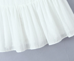 Detailed close-up of white dress showing intricate floral embroidery and ruffle hem