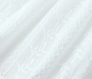 Detailed macro view of white embroidery fabric with leaf patterns on backless dress
