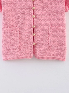 Détail d'un haut en maille rose avec boutons dorés gaufrés et tissu à mailles texturé