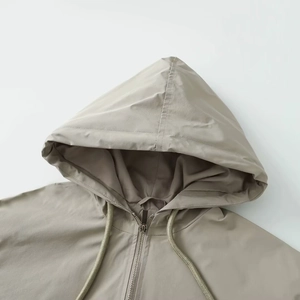 Detail view of khaki hooded jacket featuring smooth woven fabric and metal zipper closure