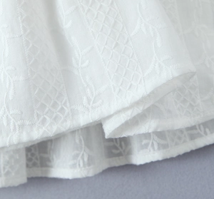Detail of white dress showing intricate leaf embroidery and geometric lattice patterns